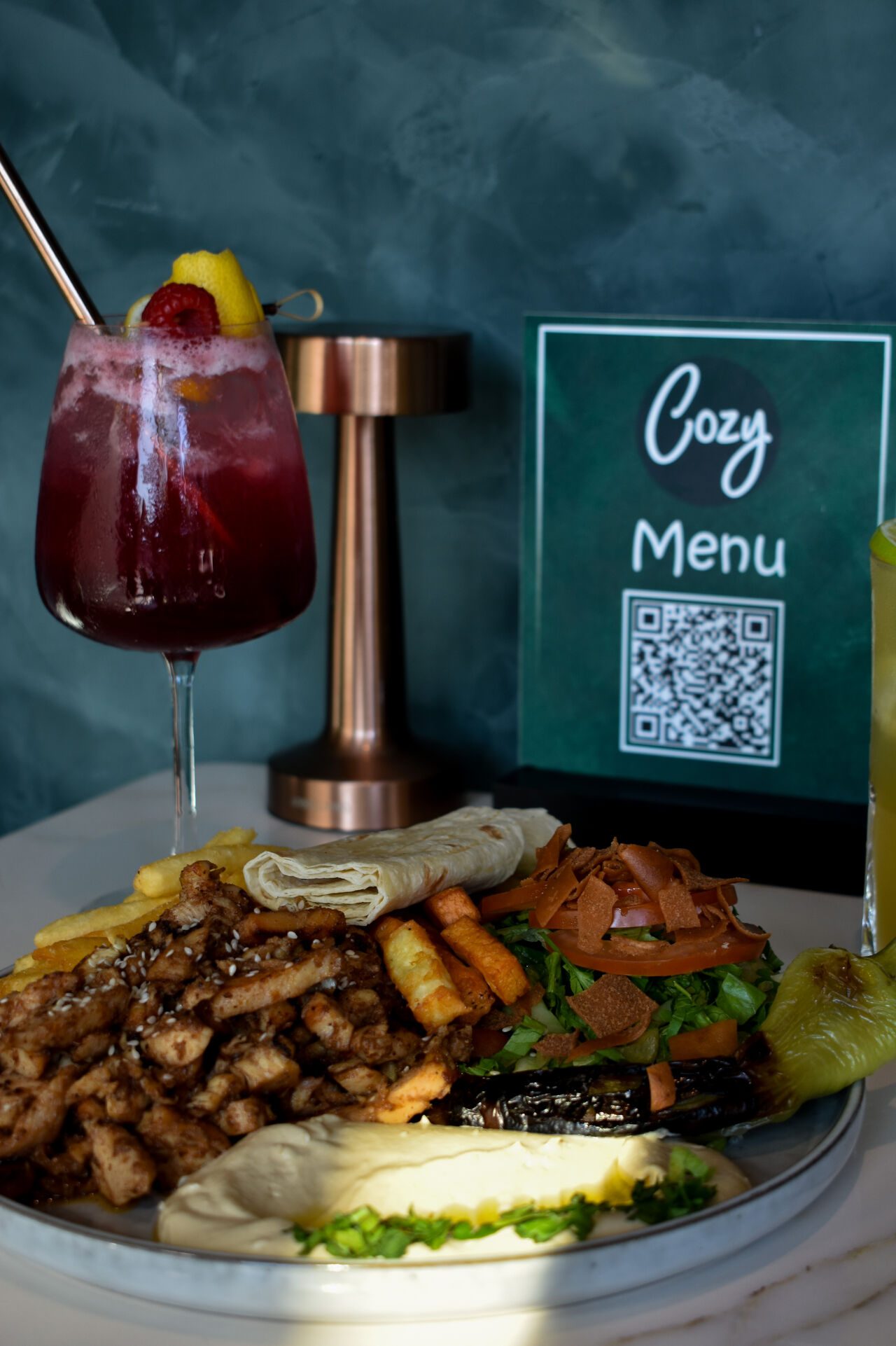Teller mit Hähnchen, Pommes, Hummus und Wrap, dazu ein roter Cocktail und die Cozy-Karte